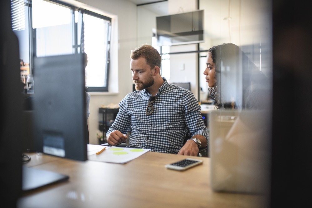 2 personen overleggen aan een bureau met een computerscherm