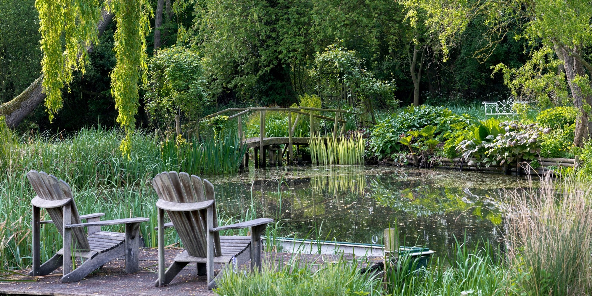 Een terras met twee houten stoelen bij een klein meertje in het bos