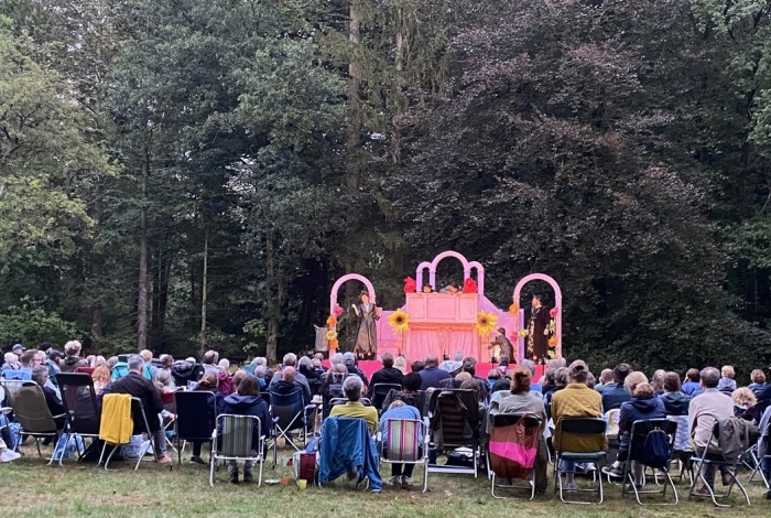 Bezoekers op stoelen kijkend naar een openlucht-voorstelling.