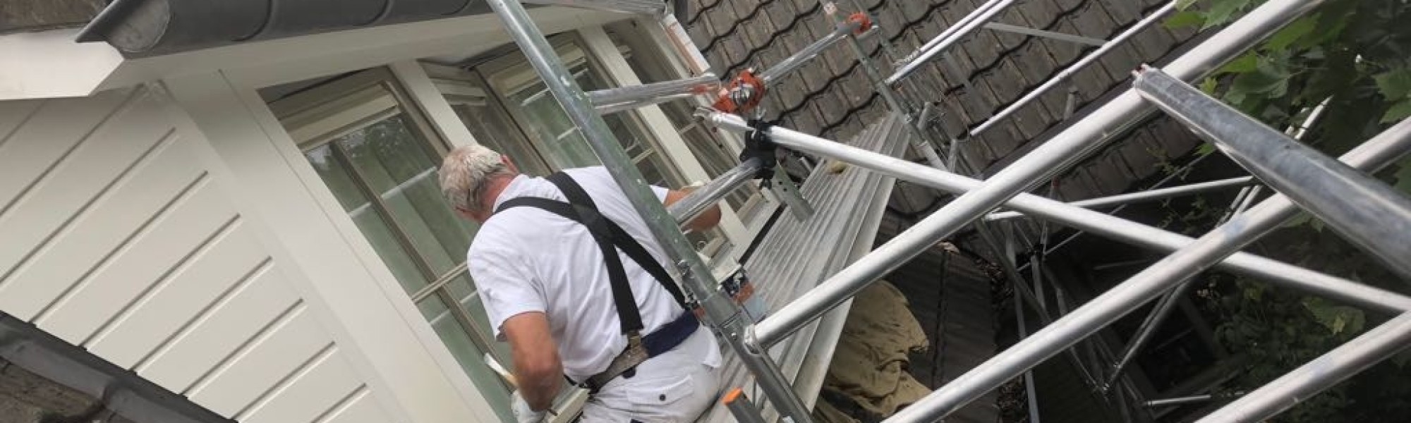 Jos Sijl die aan het schilderen is terwijl hij op een steiger zit