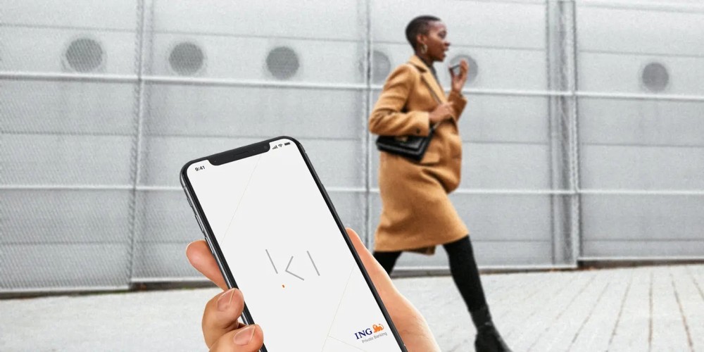 Smartphone met het logo van Ki en een dame op de achtergrond die deze telefoon in haar hand heeft