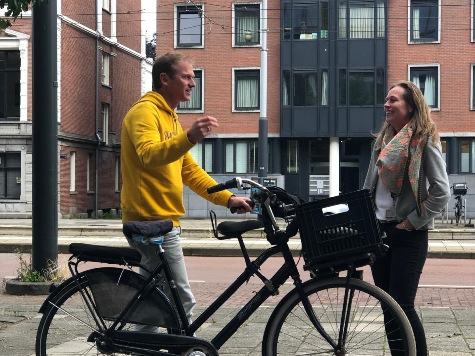 Stefanie in gesprek met Jochem. Jochem f=draagt een gele trui en ze staan op straat te praten. beide glimlachen